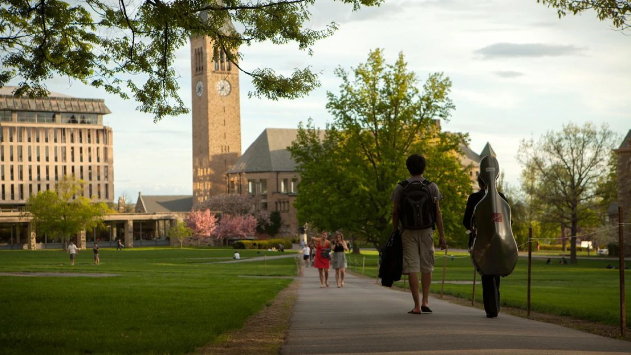 Students walk toward McGraw tower while the sun sets in the west.
